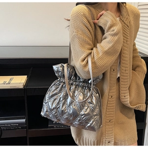Detail of silver quilted drawstring bag styled with a beige knit cardigan for winter