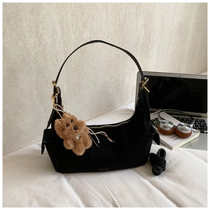 Detail of black suede hobo bag with gold hardware, brand logo and plush bear keychain