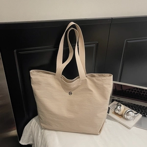 Gros plan d'un sac cabas beige avec une texture plissée subtile et un logo rond en métal