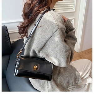 Détail du sac carré en cuir poli noir avec une boucle métallique dorée élégante