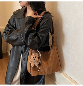 Détail d'un grand sac hobo en daim marron avec un petit pendentif de chien en peluche
