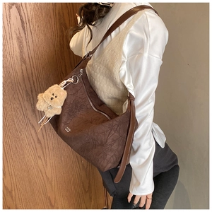 Detailed close-up of brown textured vintage shoulder bag with bear pendant and logo