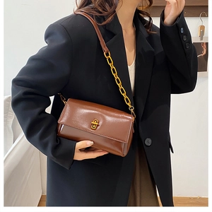 Détail d'un sac à rabat carré marron avec fermoir tournant doré et bandoulière chaîne