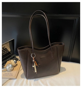 Detailed close-up of dark brown leather tote bag with FASHION embossed label and bead charm