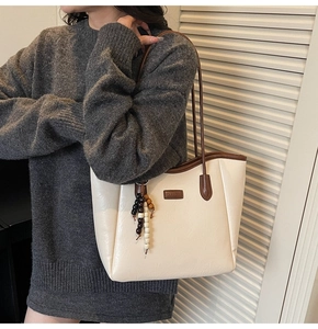 Detail view of large cream tote bag with brown straps and wooden bead pendant accessory