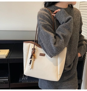 Detail of cream leather tote bag featuring a wooden bead pendant and slim brown straps