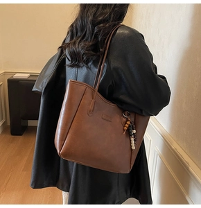 Close-up of brown leather tote bag featuring a decorative wooden beaded pendant accessory