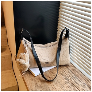 Detail of beige pleated shoulder bag featuring a cute teddy bear charm and black straps