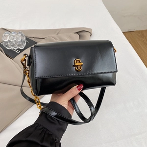 Détail d'un sac à main noir brillant avec fermoir doré et bandoulière chaîne élégante