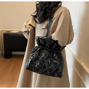 Detail of black quilted puffer shoulder bag with drawstring closure and glossy finish