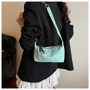Pale green suede shoulder bag with silver heart pendant on a model in a black blazer