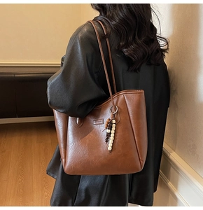 Detail of a large brown leather tote bag with a fashion logo tag and beaded charm