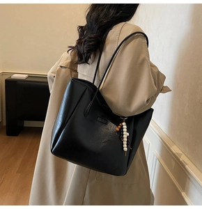 Detail view of black faux leather tote bag featuring a beaded charm and FASHION label