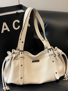 Creamy white pleated leather tote bag with silver buckle straps on a black sofa