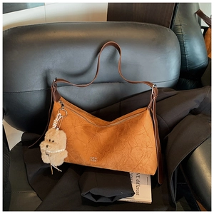 Detail showing the brown pleated texture, zipper closure and plush puppy charm on the bag