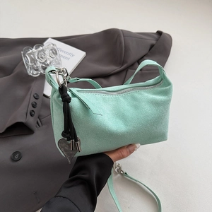 Detail of mint green suede shoulder bag featuring a metal heart charm and zipper