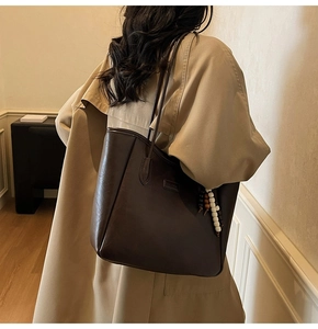 Close-up of a large coffee brown leather tote bag with elegant beaded charm and FASHION logo