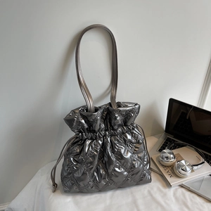 Quilted silver drawstring shoulder bag shown with lifestyle items on a white desk