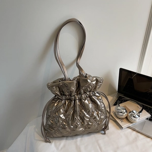 Close-up of champagne gold quilted puffer bag with drawstring on a minimalist desk