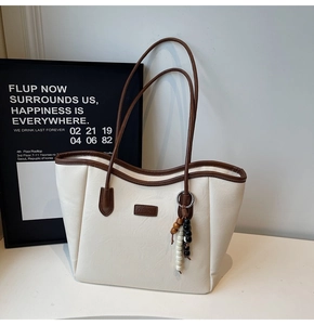Detail of off-white leather tote bag with brown trim and beaded tassel charm