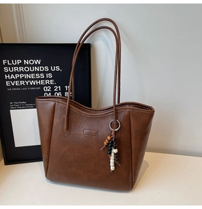 Detailed view of brown faux leather tote bag with long straps and bead tassel charm