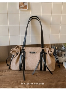 Close-up of suede tote bag with black leather straps and decorative tassel zippers