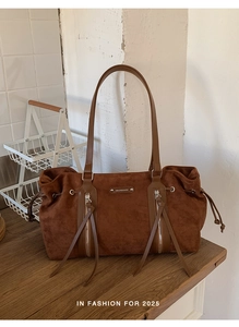 Close-up of brown suede tote bag with fringe zippers on a vintage wood table
