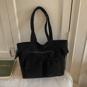 Detail of black corduroy tote bag showing metal zipper and multi-pocket functional design