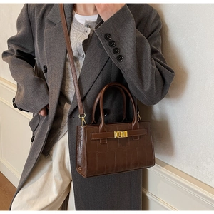 Close-up of brown croc-effect leather handbag with gold buckle on a model's grey suit