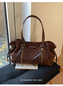 Detail of dark brown suede tote bag featuring silver vertical zippers and smooth texture