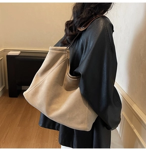 Detailed view of beige suede tote bag with leather strap worn by a model in a room