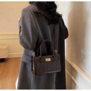 Detail of dark brown crocodile embossed handbag with gold hardware on long coat