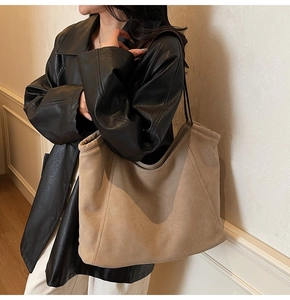Detail of large suede tote bag in khaki with leather straps on a model wearing black coat