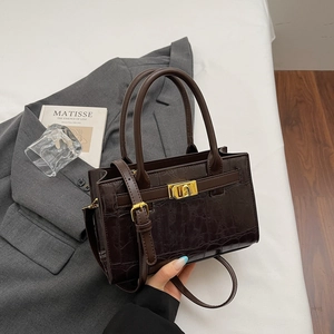 Detail of dark brown crocodile pattern handbag with gold square clasp and shoulder strap