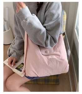 Pink nylon tote bag shown on a model sitting down to demonstrate its large size and shape