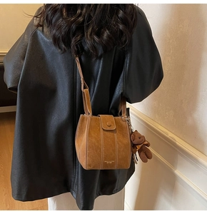Détail du sac seau marron en daim avec coutures blanches et breloque ours sur mannequin