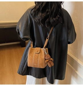 Gros plan d'un sac seau en daim marron avec surpiqûres et breloque ours en peluche