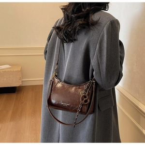 Dettaglio della borsa sottobraccio in pelle lucida marrone scuro su cappotto di lana grigio