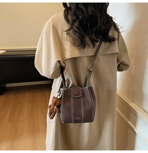 Détail du sac seau marron foncé avec coutures blanches et breloque ours en peluche