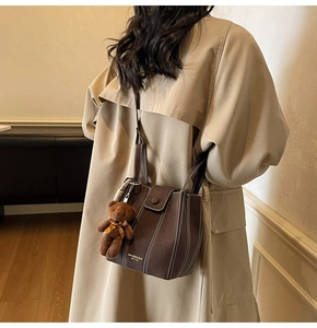 Détail du sac seau en cuir marron foncé avec coutures blanches et breloque ours