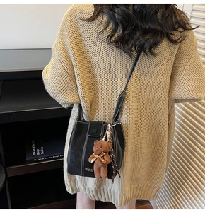Gros plan du sac seau noir avec pendentif ours sur un pull en maille beige chic