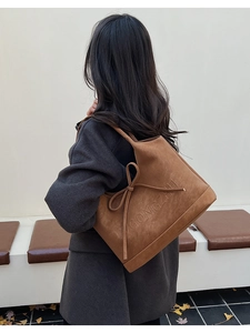 Detail of a brown suede shoulder bag with a bow decoration and embossed brand text