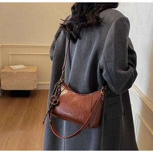 Borsa sottobraccio in pelle lucida marrone indossata sulla spalla di una modella
