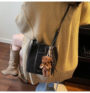 Détail du sac seau en cuir noir avec surpiqûres blanches et charm ours en peluche
