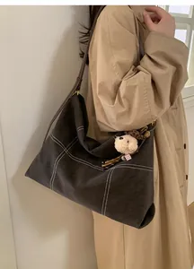 Detail of dark brown tote bag with white contrast stitching and plush bear charm decoration