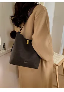Vue détaillée du grand sac seau marron foncé avec fermoir doré et logo sur un manteau