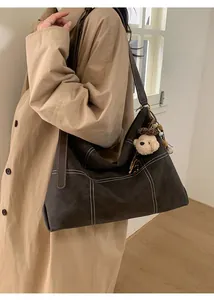 Detail of suede tote bag featuring white contrast stitching and cute plush bear charm