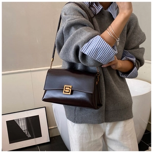 Détail d'un sac bandoulière en cuir marron foncé avec un fermoir en métal doré en forme de S