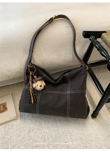 Detail of a large brown tote bag with white stitching and a cute teddy bear charm