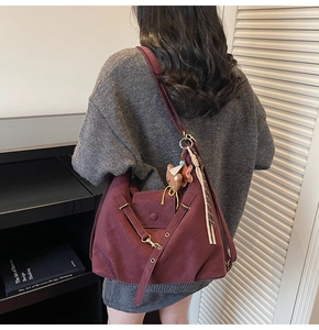 Detail of burgundy faux suede tote bag featuring a chic bear charm and striped scarf accent